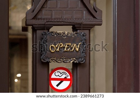 A hanging signboard with OPEN text and a no smoking sticker on the building entrance wooden door.