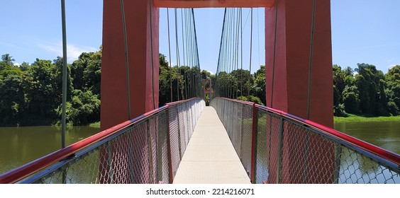 Hanging Suspension Bridge Architecture Made With Join Iorn Metal Cable Rope And Tower For Crossing Green Forest River Water. Empty And Quiet Endless Deck, Walkway Or Path Close Up View During Daytime.