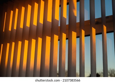 Hanging white textured vertical window slats reflecting the gold of a sunset.