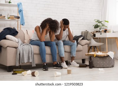 Hangover After House Party. African-american Couple Suffering From Headache, Holding Their Heads Sitting On Couch In Messy Room