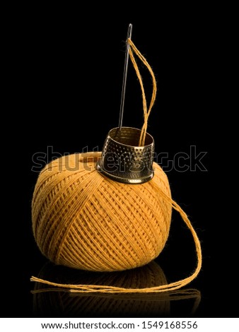 Hank of yellow threads for darning, needle and brass thimble it is isolated on black 