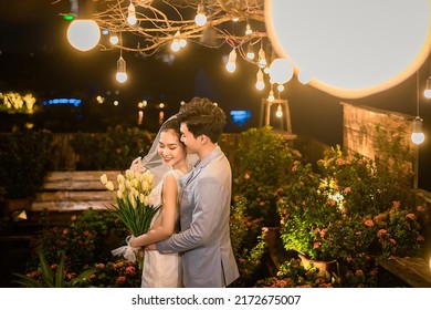 Hanoi City, Vietnam - December 2021: The Bride And Groom Are Happily Together In The Rooftop Garden Under The Romantic Shimmering Lights. The Photo Was Taken At Night.