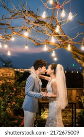 Hanoi City, Vietnam - December 2021: The Bride And Groom Are Happily Together In The Rooftop Garden Under The Romantic Shimmering Lights. The Photo Was Taken At Night.