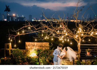 Hanoi City, Vietnam - December 2021: The Bride And Groom Are Happily Together In The Rooftop Garden Under The Romantic Shimmering Lights. The Photo Was Taken At Night.