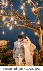 Hanoi City, Vietnam - December 2021: The Bride And Groom Are Happily Together In The Rooftop Garden Under The Romantic Shimmering Lights. The Photo Was Taken At Night.