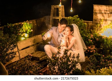 Hanoi City, Vietnam - December 2021: The Bride And Groom Are Happily Together In The Rooftop Garden Under The Romantic Shimmering Lights. The Photo Was Taken At Night.