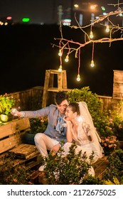 Hanoi City, Vietnam - December 2021: The Bride And Groom Are Happily Together In The Rooftop Garden Under The Romantic Shimmering Lights. The Photo Was Taken At Night.