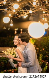 Hanoi City, Vietnam - December 2021: The Bride And Groom Are Happily Together In The Rooftop Garden Under The Romantic Shimmering Lights. The Photo Was Taken At Night.