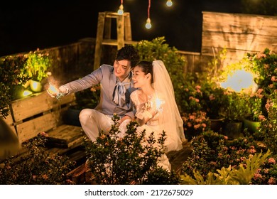 Hanoi City, Vietnam - December 2021: The Bride And Groom Are Happily Together In The Rooftop Garden Under The Romantic Shimmering Lights. The Photo Was Taken At Night.