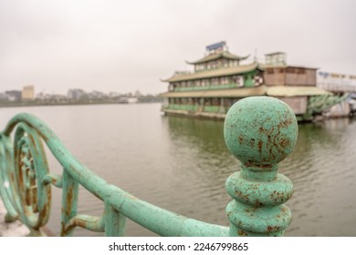 In Hanoi, Vietnam, balustrade up close, with abandoned dinner cruise ship beyond, in a beautiful waterscape on West Lake (Tay Ho). Very shallow focus for effect on cracks on left side. - Shutterstock ID 2246799865