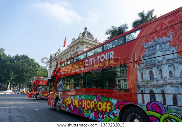 Hanoi, Vietnam - Feb 18,\
2019: Luxury city tour bus on Hanoi street with Hanoi Opera House\
on background
