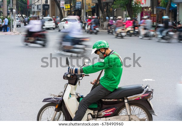 Hanoi, Vietnam - July 7, 2017: Grab motorbike driver\
waiting for customer on Ba Trieu street. Entered Vietnam in 2014,\
Grab growing fast due to cheap fare and safer than traditional\
motorbike taxi