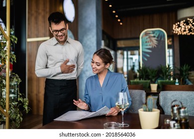 Hansome Young Waiter Showing Menu To Beautiful Female Customer In Restaurant.