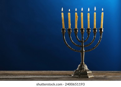 Hanukkah celebration. Menorah with burning candles on wooden table against blue background, space for text
