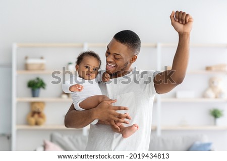 Hapiness Of Fatherhood. Joyful Young Black Dad Enjoying Spending Time With His Infant Child, Happy African American Father Holding Adorable Toddler Baby, Raising Hand And Exclaiming With Excitement