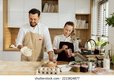 Happi Mother And Father Cooking Baking Preparing Homemade Pizza Together. Man With Beared Rolling Pizza With Hands Preparing Homemade Dough. Woman Mixing Tomato Sauce In Measuring Cup.