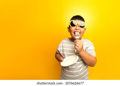 The happily boy eating sandwich by fork, yellow background. - Powered by Shutterstock