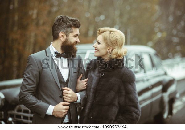 Happily married couple\
enjoying a beautiful day outdoorsat antique car, handsome wealthy\
man and his gorgeous female posing outdoors, people spending time\
together
