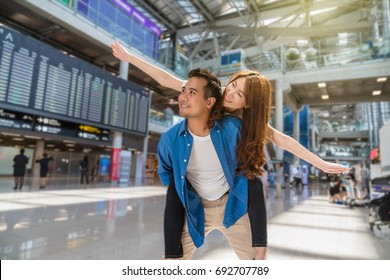 Happiness Asian Couple Traveler At The Flight Information Screen In Modern An Airport, Lifestyle Travel And Transportation Concept.