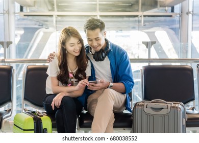 Happiness Asian Couple Traveler With Suitcases Using The Smart Phone In Modern An Airport, Travel And Transportation With Technology Concept.