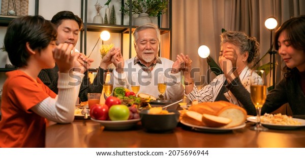happiness asian multi generation dining\
together,family holding hands and praying on thanksgiving before\
holiday dinner,grandparent grandchildren stay together in\
thanksgiving traditional dinner\
home