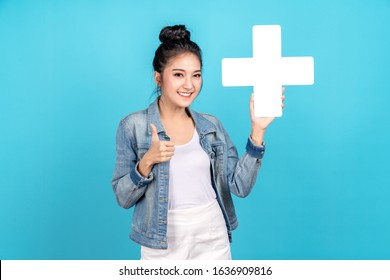 Happiness asian woman smiling, showing plus or add sign and thumb up or like on blue background. Cute asia girl wearing casual jeans shirt and showing join sign for increse and more benefit concept