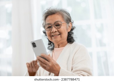 Happiness beautiful elderly asian woman with white hairs sitting on sofa using mobile phone and social media smile in cozy living room at home,Senior Wellness lifestyle at home concept - Powered by Shutterstock