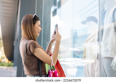 Happiness Beautiful Woman With Shopping Bag Using Cell Phone Take A Photo At Fashion Store Outside Window. Trendy Female Holding Smartphone Near Clothes Store. Women Shopping Lifestyle Fashion