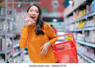 happiness cheerful exited asian female woman casual cloth hand hold empty shopping basket hand gesture announce good news or new promotion to camera,asian female smiling in supermarket groceries mall
