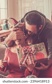 Happiness and christmas celebration concept time with man doing a gift surprise to her wife from behind closing her eyes. Happy woman receiving present for xmas holiday. December celebration together - Shutterstock ID 2396418913
