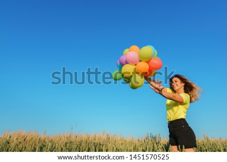 happiness concept, happy people, young woman running with multicolored balloons on summer field