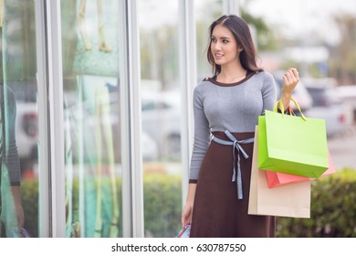 happiness, consumerism, sale and people concept - smiling young Asia woman with shopping bags at outdoor shopping mall - Shutterstock ID 630787550