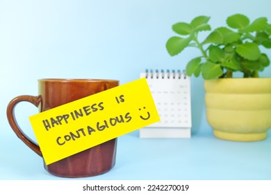 Happiness is contagious and be happy always concept. Selective focus of a cup of coffee with handwritten bright paper message note.