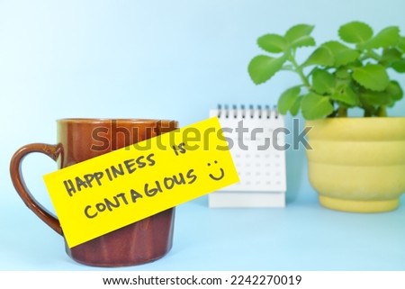 Happiness is contagious and be happy always concept. Selective focus of a cup of coffee with handwritten bright paper message note.