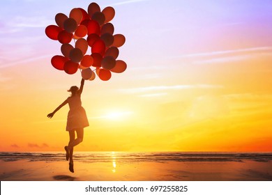 happiness or dream concept, silhouette of happy woman jumping with multicolored balloons at sunset on the beach