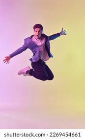 Happiness  Dynamic portrait young man in casual office fashion style jumping high over gradient yellow purple background in neon light  Wow  excitement  success concept