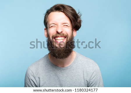 happiness enjoyment and laugh. exhilarated man with a wide grin. portrait of a young bearded hipster guy on blue background. emotion facial expression. feelings and people reaction.