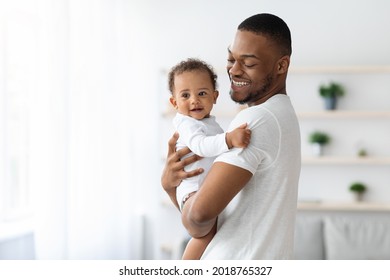 Happiness Of Fatherhood. Portrait Of Young Black Dad With Cute Little Baby On His Hands Standing Near Window At Home, Loving African American Father Spending Time With Infant Child, Copy Space