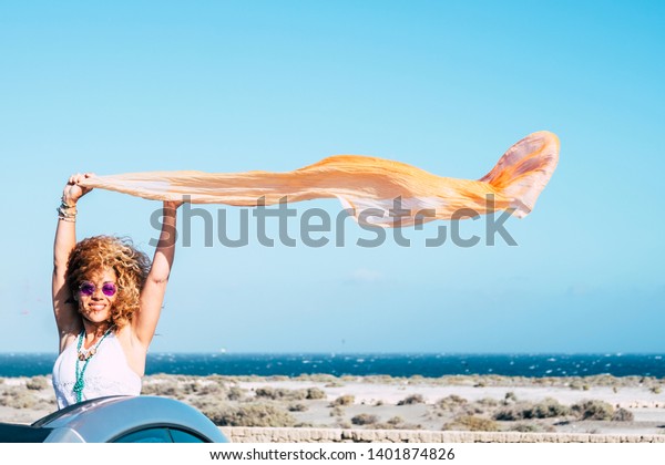 Happiness and freedom joy people concept with\
attractive middle age traveler out of a convertible car smiling and\
enjoying playing ith the wind in holiday vacation with blue sea and\
sky in background