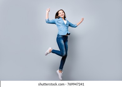 Happiness, freedom, power, motion and people concept - full length portrait of smiling young woman jumping  with raised fists over grey background