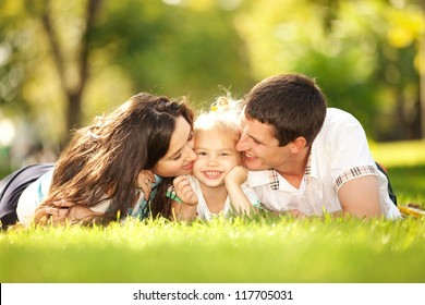 Happiness and harmony in family life. Happy family concept. Young mother and father kissing their daughter in the park. Happy family resting together on the green grass. Family having fun outdoor - Powered by Shutterstock