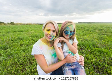 Happiness, Holi festival and holidays concept - Mother and her daughter covered with color powder smiling over nature background