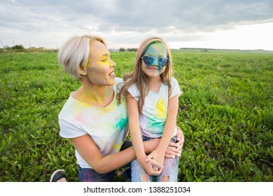 Happiness, Holi festival and holidays concept - Mother and her daughter covered with color powder smiling over nature background