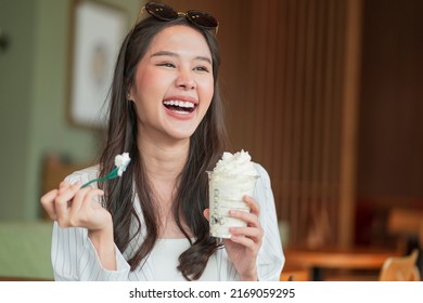 Happiness Joyful Asian Young Adult Female Woman Teasing Yummy Smiling Hand Hold Whipped Cream In Plastic Cup,enjoy Eating Asia Woman Toothy Smile While Take A Break With Glass Of Dessert In Cafe