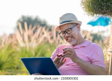 Happiness Man surprise marriage proposal online to girlfriend online thru laptop computer. Gray beard retirement mature or Senior man in Pink and Hat at Sunset. Quarantine valentines day concept.