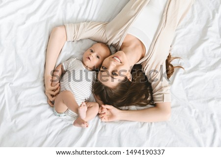 Happiness of motherhood. Smiling mother and her cute little infant baby lying on bed, top view