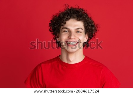Happiness. Portrait of young cheerful man in casual cloth smiling isolated over red background. Concept of feelings, youth, fashion, facial expression, emotions, lifestyle, ad