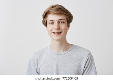 Happiness and positive human expressions. Studio shot of friendly young male student with fair hair and blue eyes laughing at good joke, smiling with braces, looking at camera with carefree smile