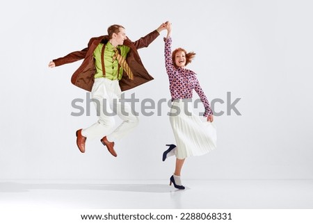 Happiness and positivity. Young smiling couple, man and woman in stylish clothes dancing retro dance against grey studio background. Art, retro style, hobby, party, movements, 60s, 70s culture concept