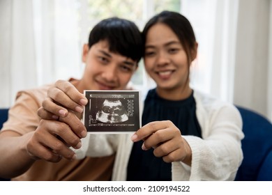 Happiness Of A Pregnant Woman And Her Husband In The Bedroom With The Ultrasound Film Of The Fetus That Shows The Results That The Child Is Healthy. Concept Of Preparing For A Family And Succession.